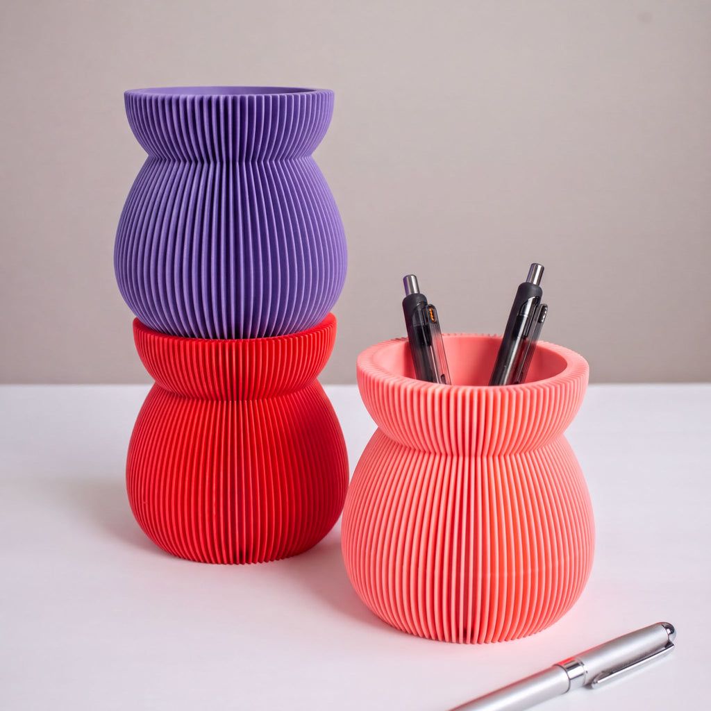 three colorful vases and a pen holder on a white surface.