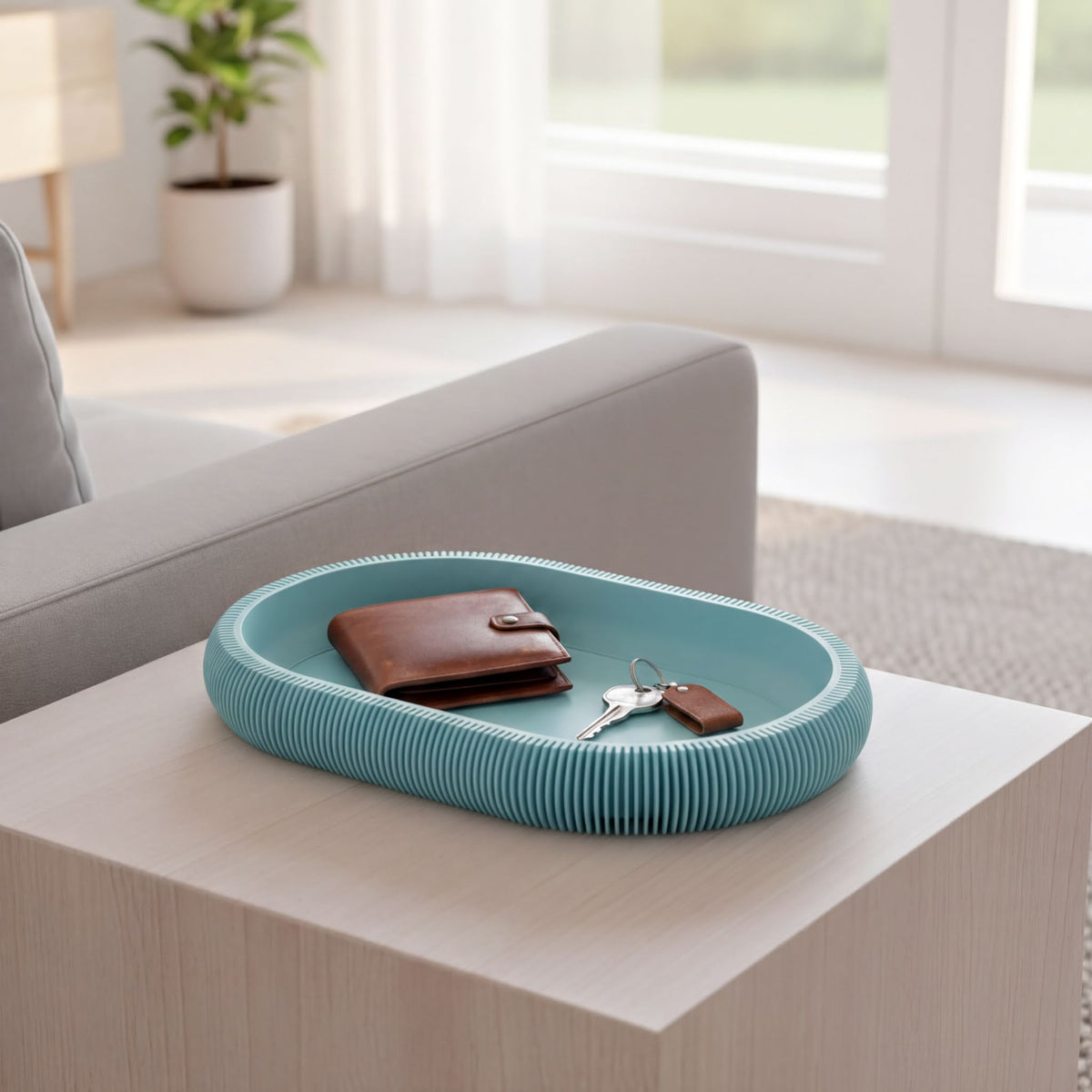 A modern, blue-colored tray with a wallet and keys placed on it, sitting on a wooden surface in a room with a window and a plant.