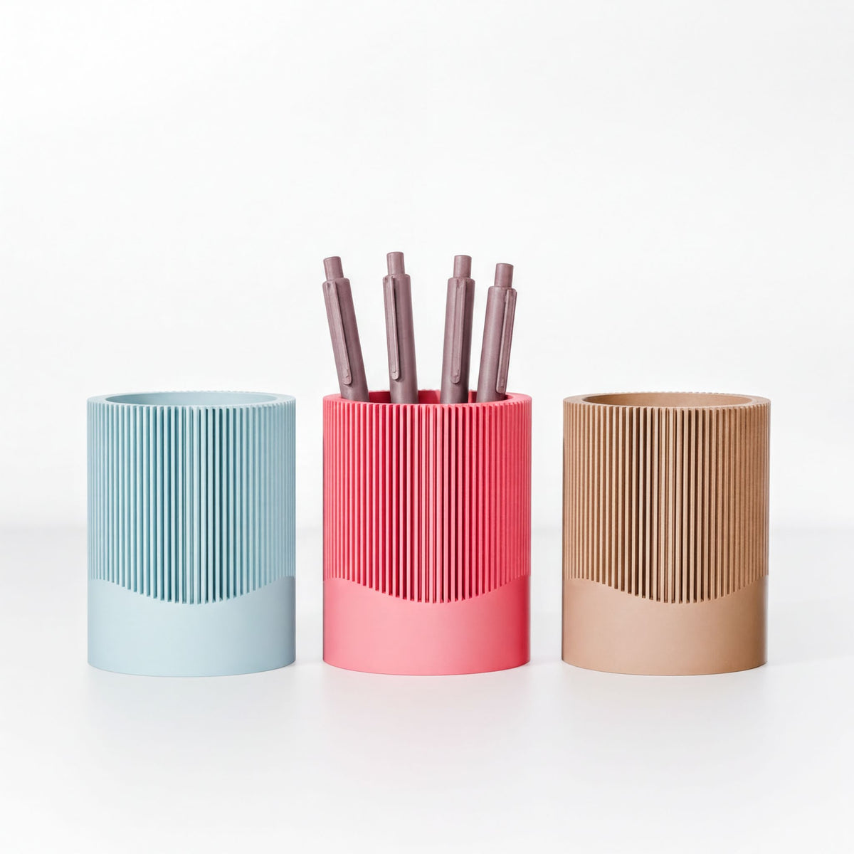 Three cylindrical containers with pens in them, each with a different color: blue, pink, and brown.
