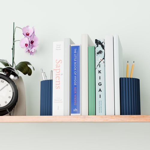 A bookshelf with a variety of books, a clock, and a vase with a purple orchid plant.