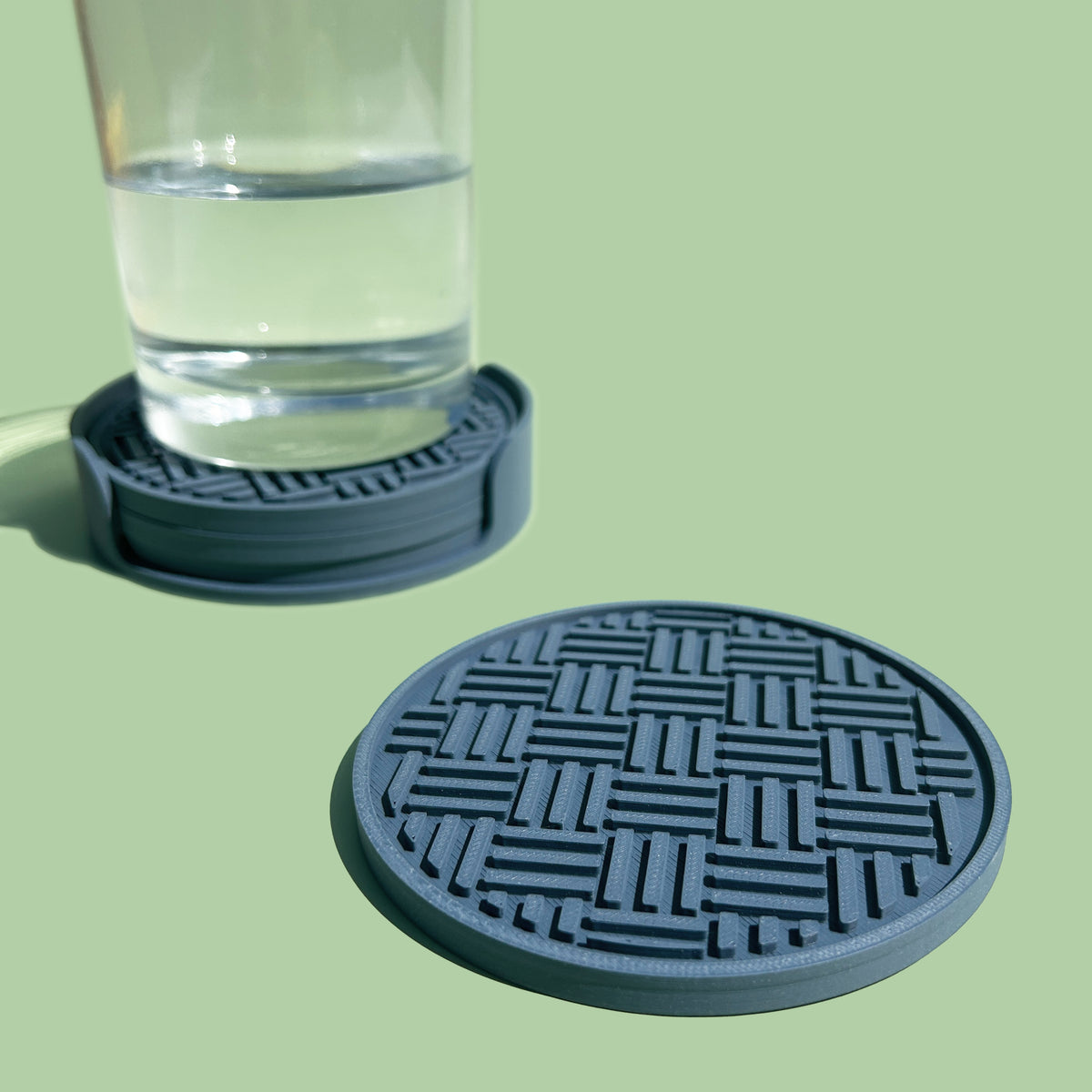a glass of water with a blue coaster in the foreground and a glass coaster in the background.