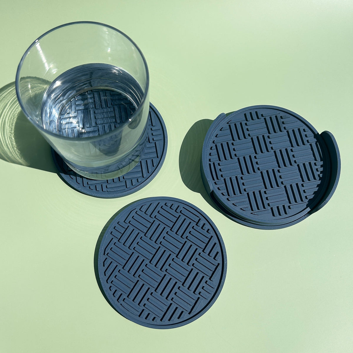a glass of water on a green background, with two coasters placed next to it.