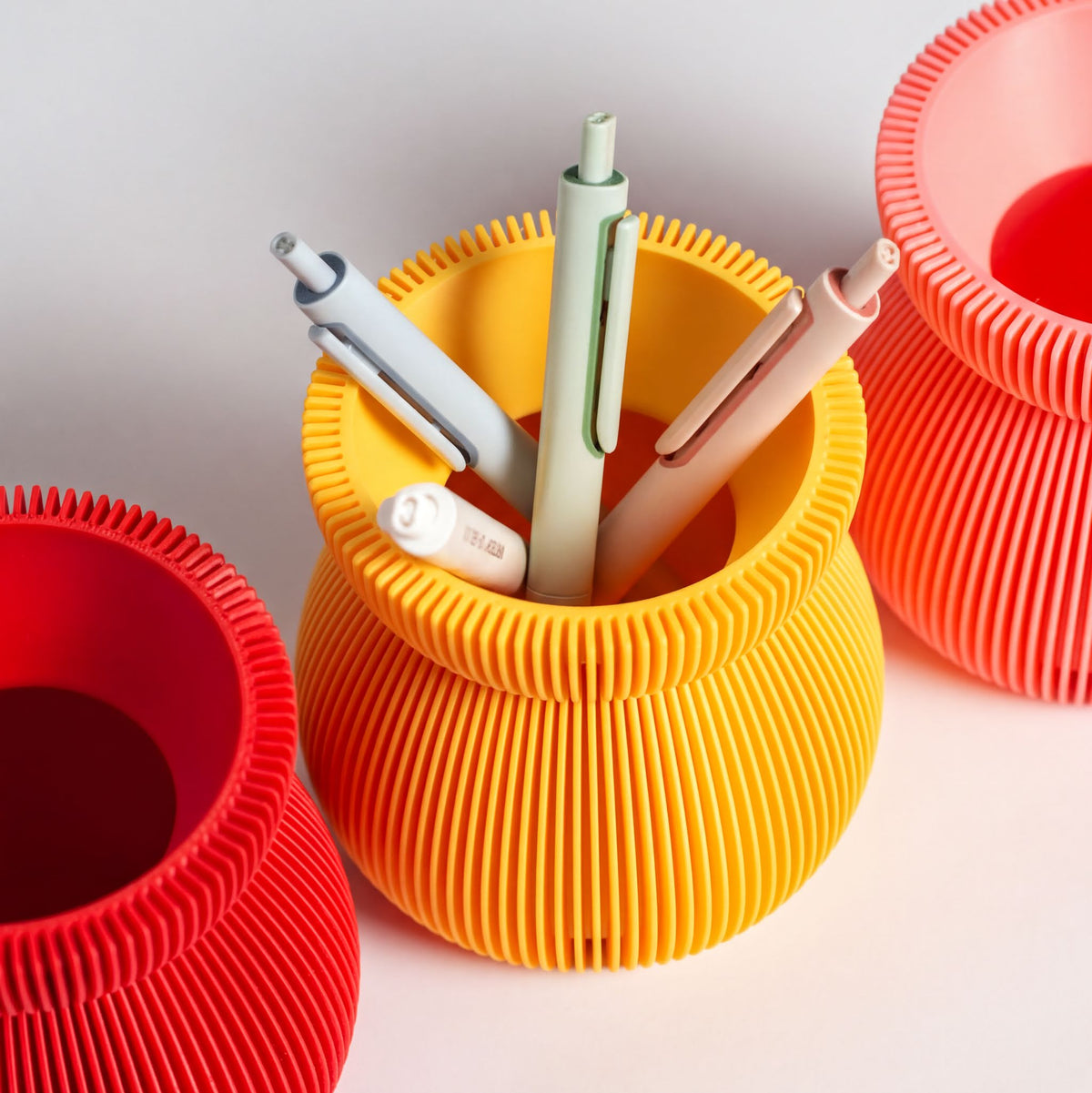 a yellow cylindrical container holding three pens of different colors - white, green, and pink.