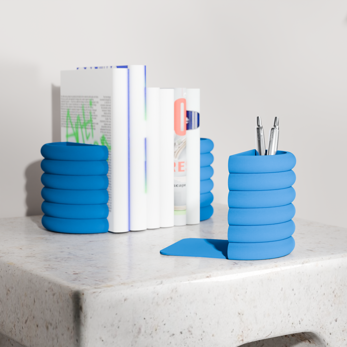 a white table with a stack of blue books and a blue cylindrical container holding pens.