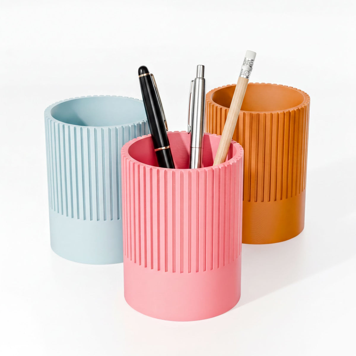 Three cylindrical containers of different colors - blue, pink, and orange - each holding a pen and a pencil.